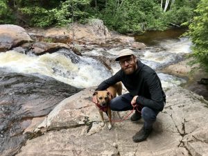 Photo of Matthew Locke smiling with a dog in front of a river